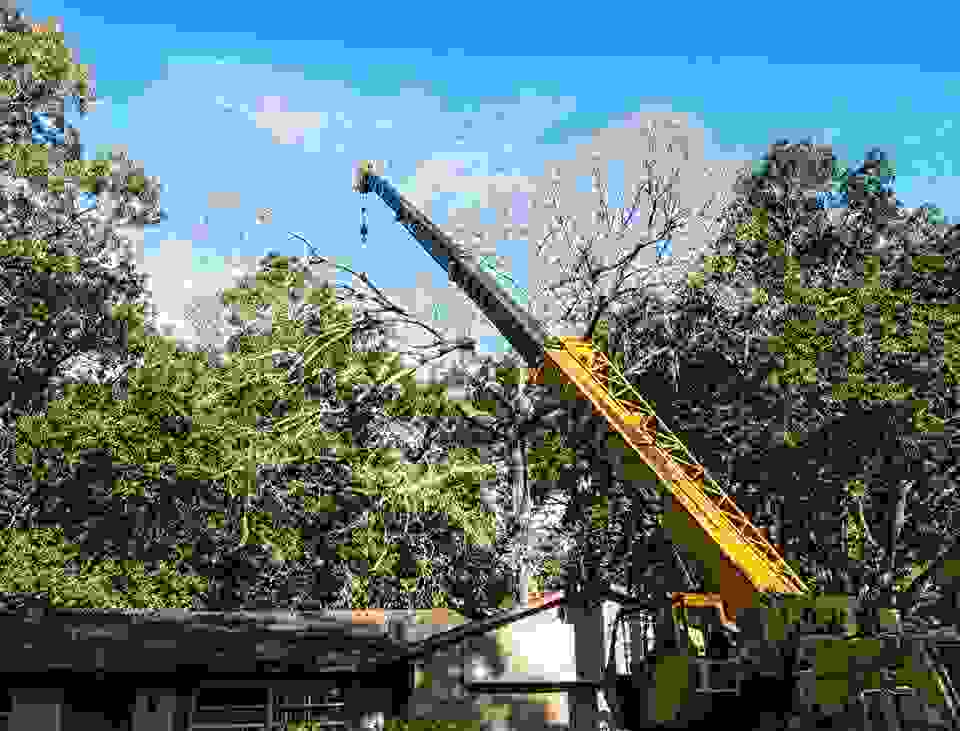 A crane extending over a house lifting a large section of canopy.